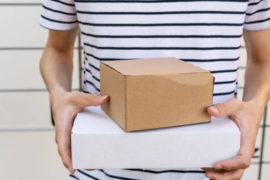 Person holding a cardboard box. A man with a box in his hands near the self-service mail terminal. Parcel delivery machine. Mail delivery and post service, online shopping, e commerce concept