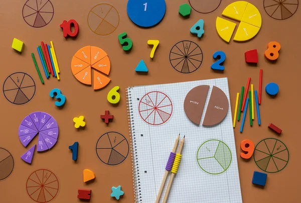 Kesirler, cetveller, kalemler, kahverengi arka planda not defteri. Matematik ve okul için malzeme seti. Okula dönüş, eğlenceli eğitim konsepti.