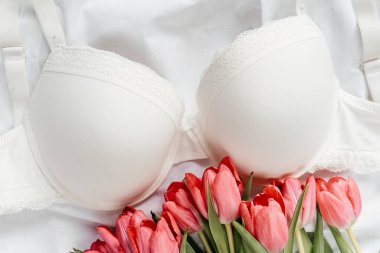 Beyaz sutyen, yatakta pembe laleler. Kadınlar yumuşak iç çamaşırları, iç çamaşırları. Üst Manzara, kapat. Düz yatak, güzellik blogu ya da sosyal medya minimum konsepti. Sevgililer Günü, Kadınlar Günü hediyesi.