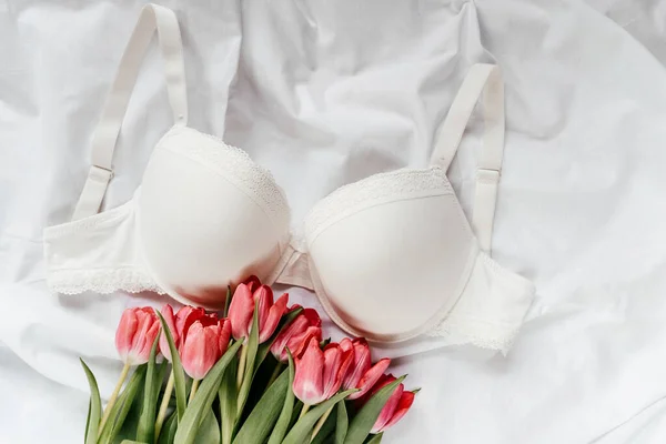 stock image White bra, pink tulips on the bed. Women tender lingerie, underwear. Top view, close up. Flat lay, beauty blog or social media minimal concept. Present for Valentines, Womens day