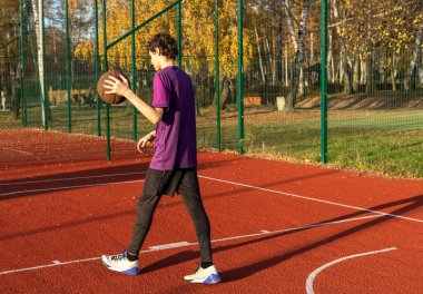 Sahada top oynayan tişörtlü hoş bir genç kız. Stadyumda koşan bir genç. Spor, hobi, erkekler için aktif yaşam tarzı