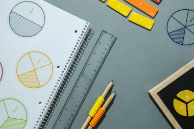 Kesirler, cetveller, kalemler, gri arka planda not defteri. Matematik ve okul için malzeme seti. Okula dönüş, eğlenceli eğitim konsepti.