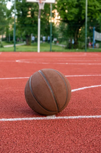 地上のバスケットボールボール 赤いコートの上のクローズアップボール 路上や屋内コートでのバスケットボール 人のいないスポーツ用具 ミニマリズム テンプレート スポーツの背景 — ストック写真