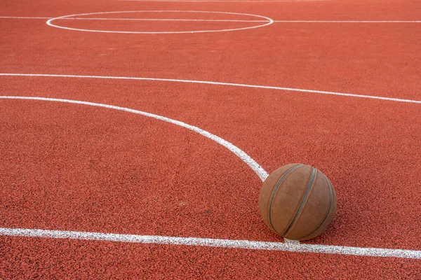 地上のバスケットボールボール 赤いコートの上のクローズアップボール 路上や屋内コートでのバスケットボール 人のいないスポーツ用具 ミニマリズム テンプレート スポーツの背景 — ストック写真