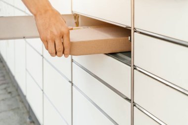 Posta terminalinin yanında elinde kutu olan bir adam. Paket teslimat makinesi. Elinde bir karton kutu tutan kişi. Posta ve posta servisi, online alışveriş, e-ticaret konsepti