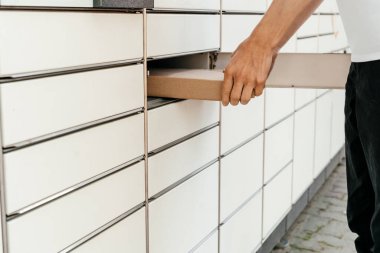 Posta terminalinin yanında elinde kutu olan bir adam. Paket teslimat makinesi. Elinde bir karton kutu tutan kişi. Posta ve posta servisi, online alışveriş, e-ticaret konsepti