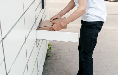 Posta terminalinin yanında elinde kutu olan bir adam. Paket teslimat makinesi. Elinde bir karton kutu tutan kişi. Posta ve posta servisi, online alışveriş, e-ticaret konsepti