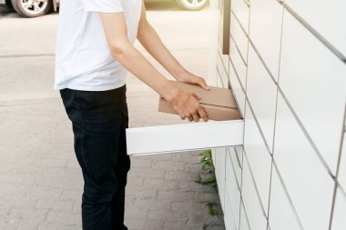 Posta terminalinin yanında elinde kutu olan bir adam. Paket teslimat makinesi. Elinde bir karton kutu tutan kişi. Posta ve posta servisi, online alışveriş, e-ticaret konsepti