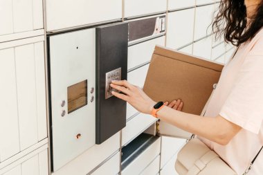 Posta terminalinin yanında elinde kutu olan bir kadın. Paket teslimat makinesi. Elinde bir karton kutu tutan kişi. Posta ve posta servisi, online alışveriş, e-ticaret konsepti