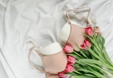 Yatakta laleli yumuşak, beyaz dantelli sütyen. Kadınlar yumuşak iç çamaşırları, iç çamaşırları. Üst Manzara, kapat. Düz yatak, güzellik blogu ya da sosyal medya minimum konsepti. Sevgililer Günü, Kadınlar Günü hediyesi.