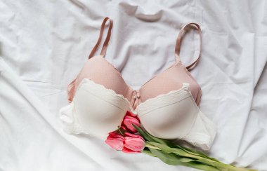 Yatakta laleli yumuşak, beyaz dantelli sütyen. Kadınlar yumuşak iç çamaşırları, iç çamaşırları. Üst Manzara, kapat. Düz yatak, güzellik blogu ya da sosyal medya minimum konsepti. Sevgililer Günü, Kadınlar Günü hediyesi.