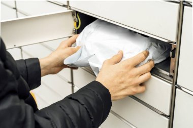 A man with a box in his hands near the self-service mail terminal. Parcel delivery machine. Person holding a cardboard box. Mail delivery and post service, online shopping, e commerce concept clipart