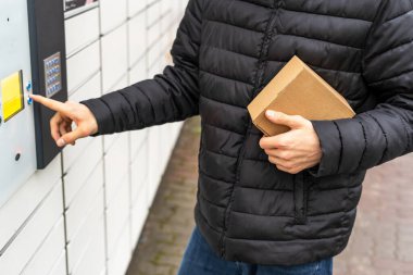Posta terminalinin yanında elinde kutu olan bir adam. Paket teslimat makinesi. Elinde bir karton kutu tutan kişi. Posta ve posta servisi, online alışveriş, e-ticaret konsepti