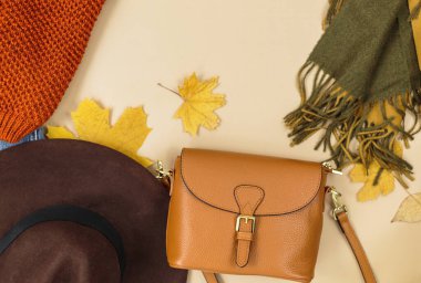 Turuncu deri kadın çantası, örgü süveter, eşarp bej kahverengi arka planda sonbahar yaprakları. Moda sonbahar aksesuarları. Samimi kıyafet.
