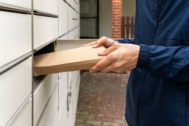 Posta terminalinin yanında elinde kutu olan bir adam. Paket teslimat makinesi. Elinde bir karton kutu tutan kişi. Posta ve posta servisi, online alışveriş, e-ticaret konsepti