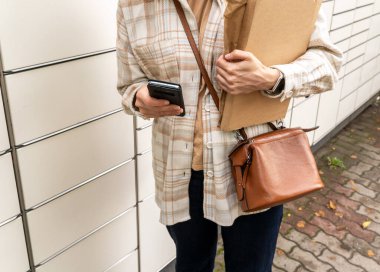 Posta terminalinin yanında elinde kutu olan bir kadın. Paket teslimat makinesi. Elinde bir karton kutu tutan kişi. Posta ve posta servisi, online alışveriş, e-ticaret konsepti