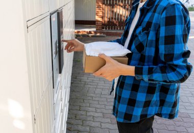 Posta terminalinin yanında elinde kutu olan bir adam. Paket teslimat makinesi. Elinde bir karton kutu tutan kişi. Posta ve posta servisi, online alışveriş, e-ticaret konsepti