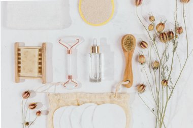 Kristal gül kuvars ve masaj aleti yeşim taşı beyaz arka planda kuru çiçeklerle yüz silindiri. Yaş karşıtı masaj, spa, sağlık, evde doğal yüz gerdirme araçları. Model