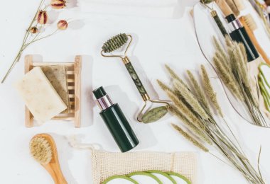 Kristal gül kuvars ve masaj aleti yeşim taşı beyaz arka planda kuru çiçeklerle yüz silindiri. Yaş karşıtı masaj, spa, sağlık, evde doğal yüz gerdirme araçları. Model