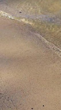 Sahil boyunca uzanan altın kum, yumuşak dalgalar ritmik bir şekilde dolaşırken sıcak öğleden sonra güneş ışığında huzurlu bir atmosfer yaratır..