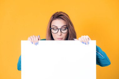 Beyaz tahtanın arkasında yakın plan kadın ve boş alana bakıyor, sarı arka planda izole edilmiş mavi deri ceket giyiyor. Kafasının yanında mesaj atmak için boş alan gösteren güzel bir kız. Stüdyo çekimi