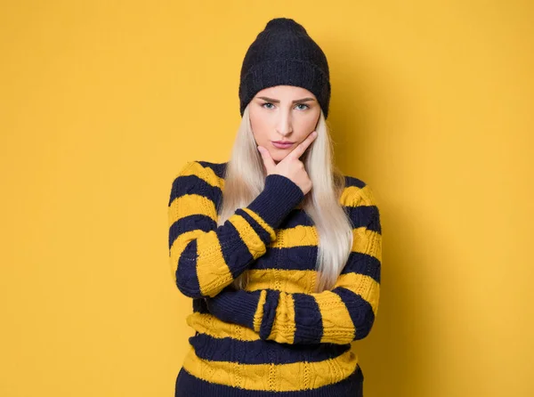 厳格な若い女性は モデルのウールキャップとセーターを着て 黄色の背景に隔離された 嫉妬深い可愛い女だ スタジオショット — ストック写真