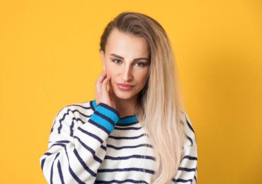 Sarı arka planda izole edilmiş güzel bir kadın. Güzel bir kız ellerini yanaklarından ayırmıyor. Stüdyo çekimi