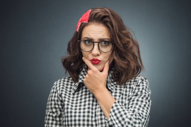 Elleri çenesinde, koyu gri arka planda kızgın yüz ifadesine bakan katı bir kadın. Şüpheyle bakan kıskanç kadın. Stüdyo çekimi