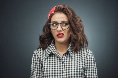 Koyu gri, siyah arkaplan üzerine sinirli genç bir kadın. Surat asan hoşnutsuz kız. Stüdyo çekimi