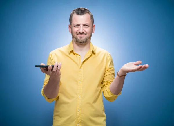 Irritated Young Man Holding Mobile Phone Blue Background Dresses Yellow — Stock Photo, Image