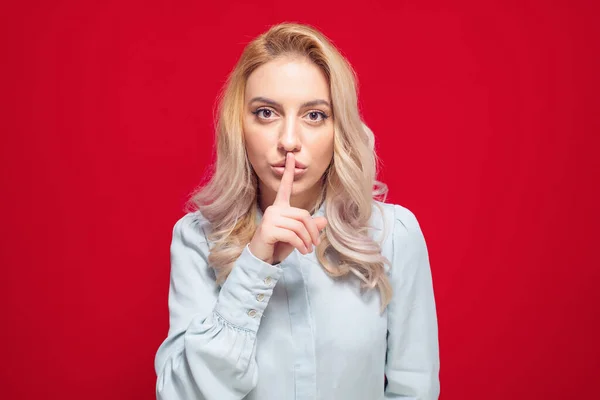别吵了女人把手指放在嘴唇上 保守秘密的概念 隔离在红色的背景上 工作室拍摄 图库照片