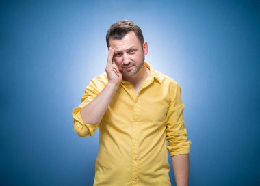 Mavi arka planda kameraya bakan yorgun bir adam, sarı gömlekli. Uykulu suratlı bitkin bir adam. Stüdyo çekimi