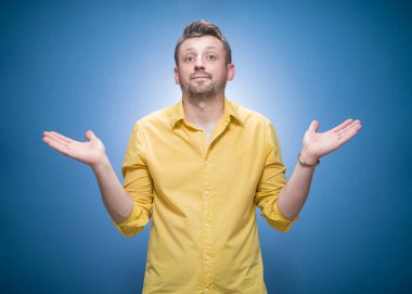 Çözüm. Kolları açık genç adam mavi arka plan yerine sarı gömlekli birini seçmene izin veriyor. Stüdyo çekimi