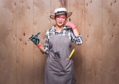 Ara beni, elinde budama makası tutan bahçıvan kadın telefonda konuşurken ahşap arka planda kameraya bakıyor. Bahçıvan kadın telefonda budama makası tutuyor. Stüdyo çekimi