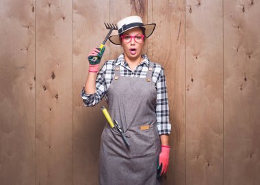 Etkileyici bahçıvan kadın elinde tırmıkla kameraya bakıyor ve stüdyoda ahşap arka planda ne olduğunu söylüyor. Stüdyo çekimi