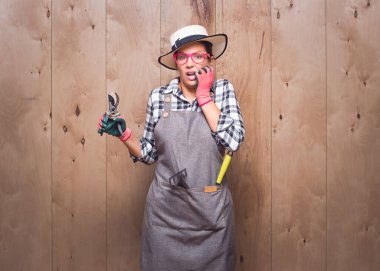 Tırnak yiyen budama makası tutan ürkek genç bahçıvan kadın stüdyodaki ahşap arka planda korkunç bir kazaydı. Korkmuş kadın. Stüdyo çekimi