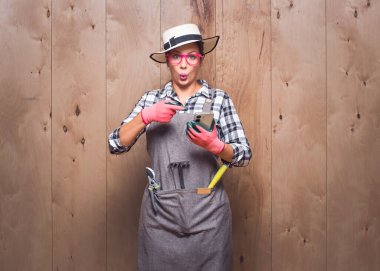 Şaşırmış genç bahçıvan kadın telefonuna stüdyodaki ahşap arka planla ilgili beklenmedik bir haber veriyor. Şaşırtıcı kadın çiftçi. 5G konsepti. Stüdyo çekimi