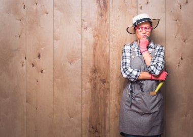 Tarafını arayan, somurtkan yüz ifadesiyle düşünen, genç bahçıvan kadın stüdyodaki ahşap arka planda yazı için yer kopyalayan şüpheli bir kadın. Stüdyo çekimi