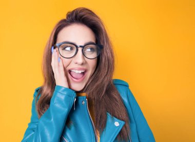 Mavi deri ceket giyen, sarı arka planda izole edilmiş, şaşırmış bir kadının yüzünü kapatın. Şaşkın kız. Şaşırtma konsepti. Stüdyo çekimi