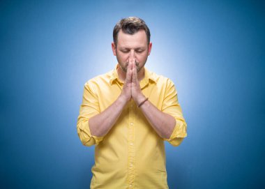 Sakin, mavi arka planda gözleri kapalı, sarı gömlekli genç bir adam. Meditasyon konsepti. Stüdyo çekimi