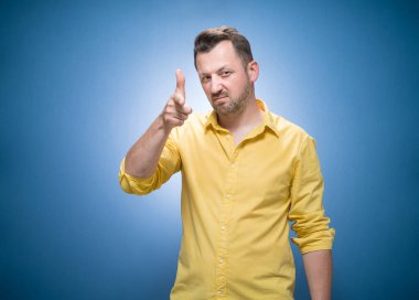 Yarım uzunluktaki bir adam seni vurmaya hazırlanıyor mavi arka planda silah hareketi yapan, sarı gömlekli bir adam. Stüdyo çekimi