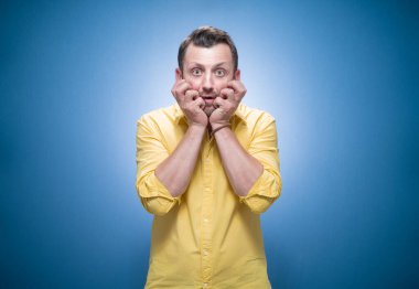 Yanlışlık. Korkmuş genç adam mavi arka planda sana bakıyor, sarı gömlekli. Stüdyo çekimi