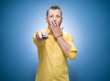 Şok olmuş bir adam elinde uzaktan kumandayla mavi arkaplanda korku filmlerini arıyor, sarı tişörtlü giyiniyor. Korkmuş bir adamın ön görüntüsü televizyon gösteriyor. Stüdyo çekimi