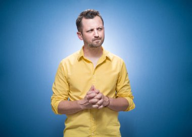 Dikkatli ol, kaşlarını çatmış, çözüm arayan mavi arka plandaki sorunları düşünen, sarı tişörtlü adam. Stüdyo çekimi