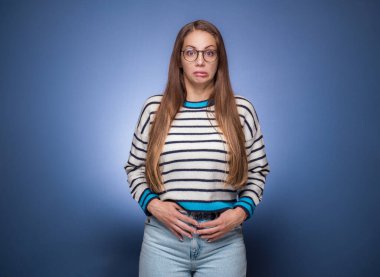 Kafası karışmış genç bir kadın, mavi arka planda izole edilmiş. Suratı asık komik bir kız. Stüdyo çekimi