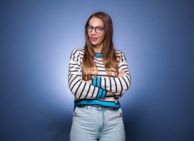 Kollarını çapraz tutan, mavi arka planda izole edilmiş şüpheli ve tatminsiz bir kadın. Kızgın ve sinirli yüz, şüpheci ve şüpheli ifade. Stüdyo çekimi