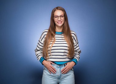 Gülümseyen yüz ifadesi olan güzel bir kız, mavi arka planda soyutlanmış. Gülümseyen genç kadın. Stüdyo çekimi