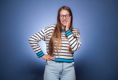 Diş ağrısı. Dişleri ağrıyan genç bir kadın, mavi arka planda izole edilmiş. Stüdyo çekimi