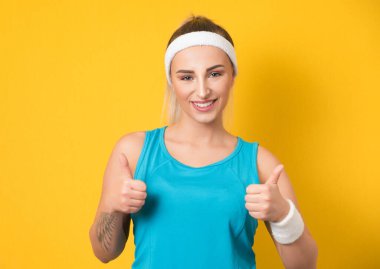 Spor giysileri giyen, hayat dolu genç bir kadın. Spor giyim, konsept gibi, sarı arka planda izole edilmiş. Evet, el kol hareketi, iyi iş çıkarmanın şarkıları. 80 'lerin stili. Stüdyo çekimi