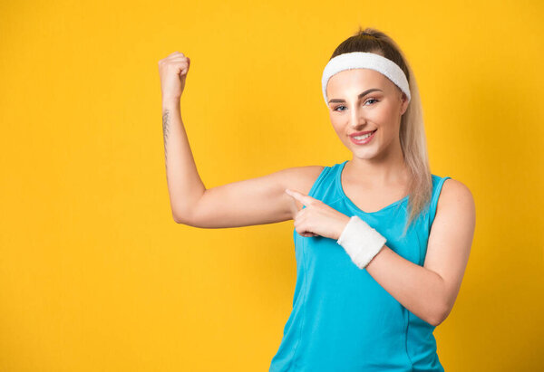 Smile sporty girl shows her biceps after training, isolated on yellow background. Half-length athletic female person. 80s styling. Studio shot